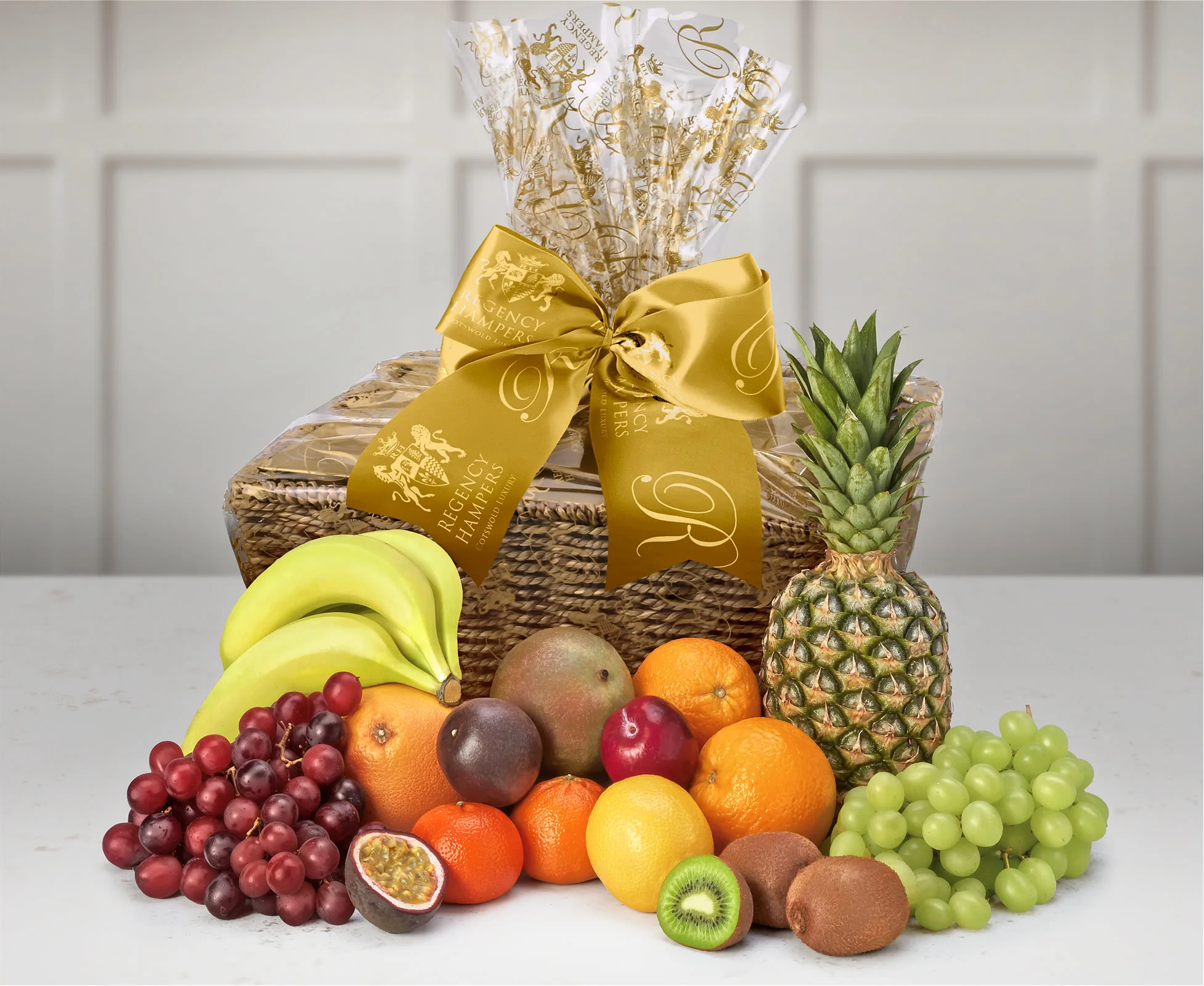 A fruit basket with various bananas, grapes, pineabbles, kiwis, oranges and various other fruits.